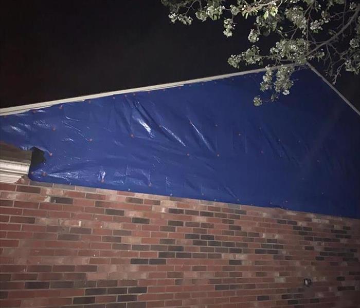 Tarp covering one side of a home that is missing a part of the wall.