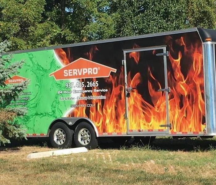 A SERVPRO trailer detailed with flames and the logo parked in the grass.