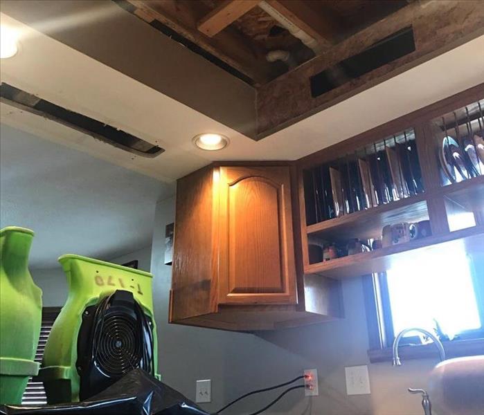 Air movers dry a kitchen with a missing ceiling due to water damage.