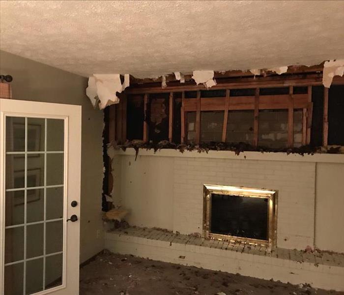 Above the fireplace in an empty living room, the entire wall has been destroyed, exposing the outside.
