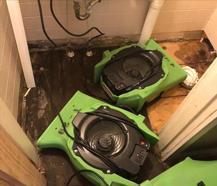 Two air movers sit in a restroom with its floor removed from water damage.
